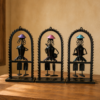 Set of three handcrafted Rajasthani-style metal figurine wall decor panels with colorful traditional attire, displayed on a table and mounted on a wall.