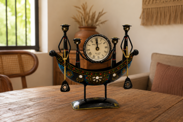 Decorative handcrafted metal boat-shaped table clock with colorful traditional Indian artwork, displayed on a wooden living room table.